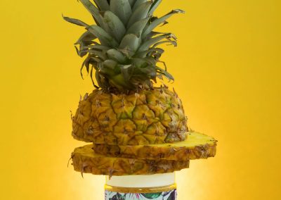 pineapple body scrub between a pineapple in front of glowing yellow background